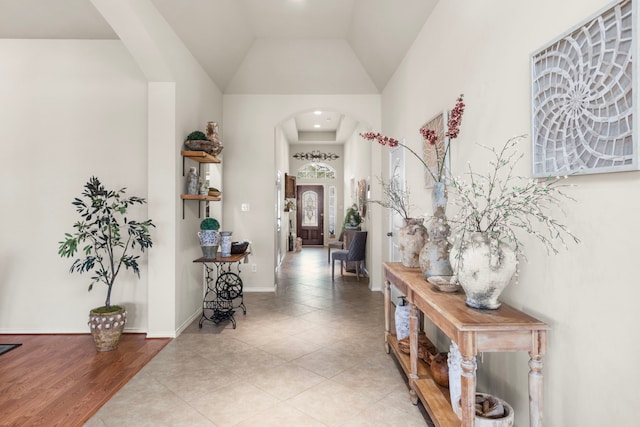 interior space with light tile patterned floors, baseboards, arched walkways, and high vaulted ceiling