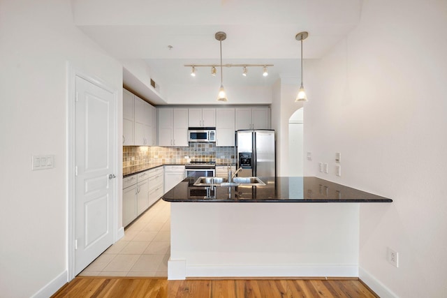 kitchen featuring a peninsula, a sink, appliances with stainless steel finishes, backsplash, and pendant lighting