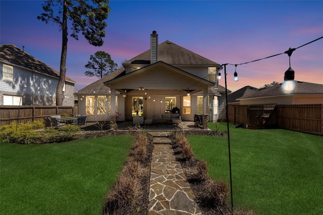 back of house featuring a fenced backyard, a lawn, a chimney, and a patio