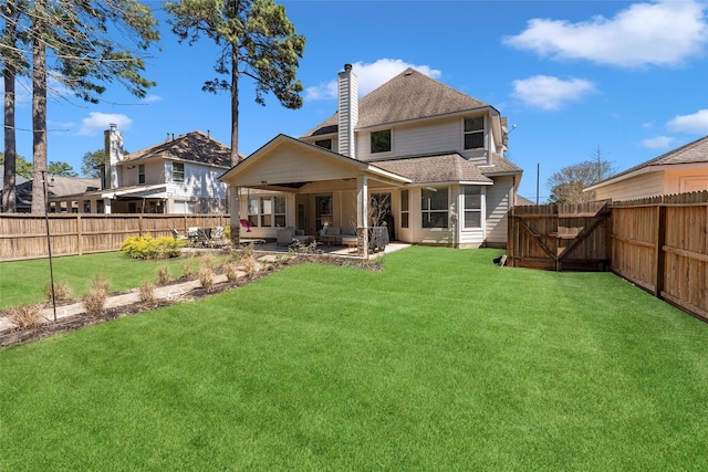 rear view of property featuring a fenced backyard, a chimney, a patio, and a yard