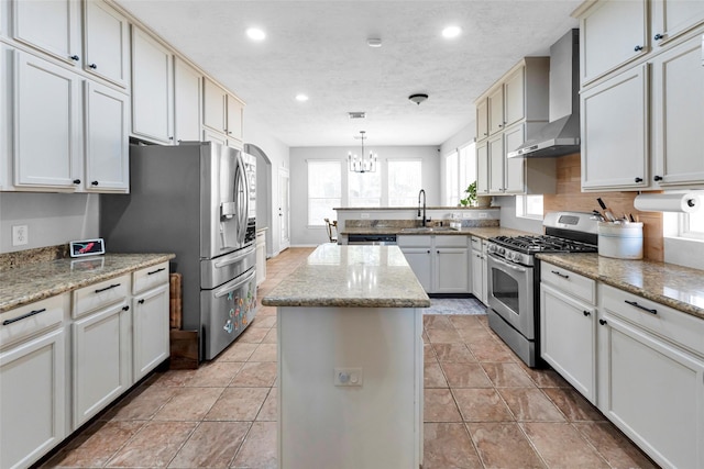 kitchen with wall chimney exhaust hood, a center island, a peninsula, stainless steel appliances, and a sink