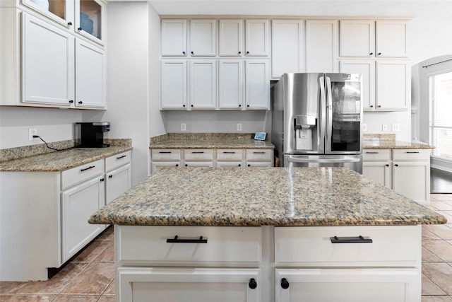 kitchen with light tile patterned floors, a kitchen island, light stone counters, and stainless steel fridge with ice dispenser