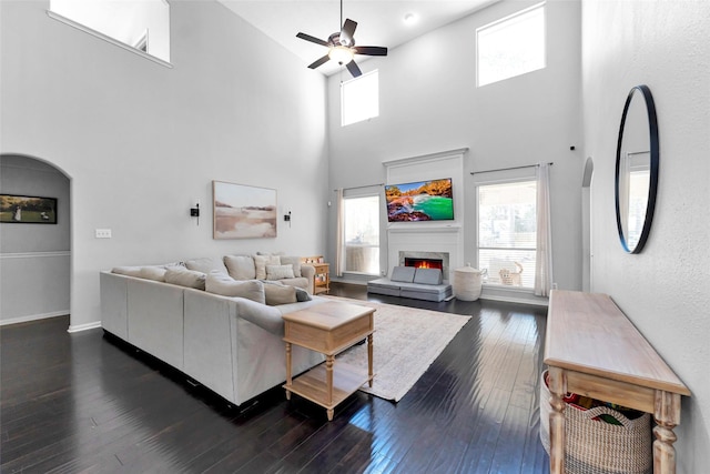 living room featuring arched walkways, ceiling fan, dark wood-type flooring, a premium fireplace, and baseboards