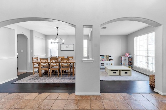 tiled dining room with arched walkways, an inviting chandelier, visible vents, and baseboards