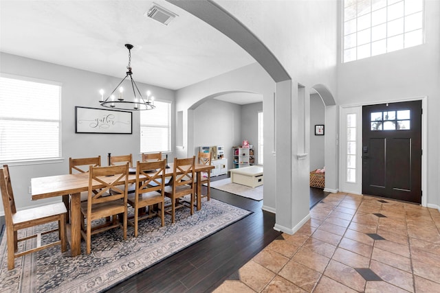 dining space featuring baseboards, visible vents, arched walkways, wood finished floors, and a notable chandelier