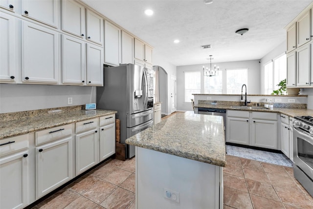 kitchen featuring a center island, arched walkways, appliances with stainless steel finishes, a sink, and a peninsula