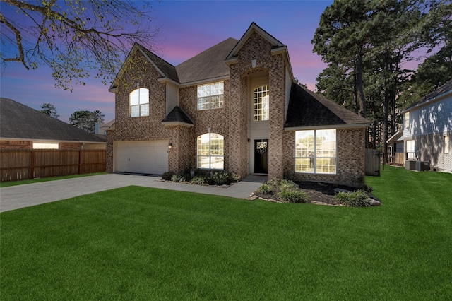 view of front of home with driveway, brick siding, a lawn, and fence