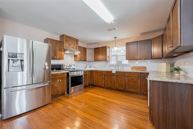 kitchen with stainless steel appliances, visible vents, decorative backsplash, light wood-style floors, and under cabinet range hood