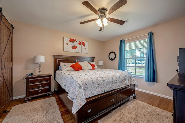 bedroom featuring a barn door, visible vents, a ceiling fan, baseboards, and dark wood finished floors