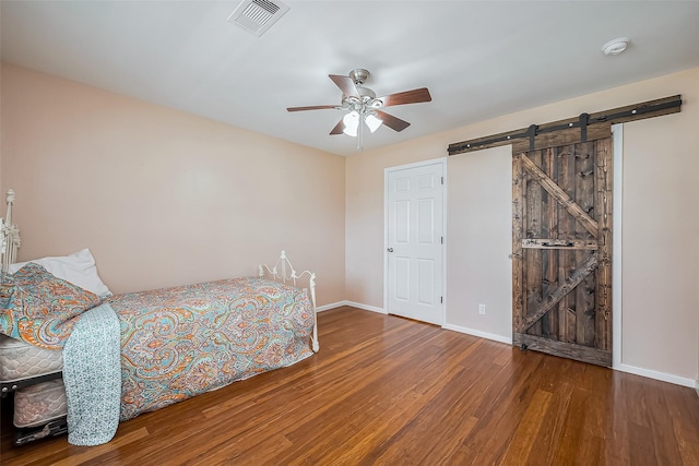 bedroom with a barn door, wood finished floors, a ceiling fan, visible vents, and baseboards