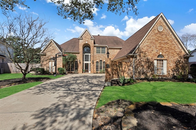 view of front facade with a front yard, fence, a shingled roof, concrete driveway, and brick siding