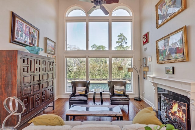 living area featuring a towering ceiling, wood finished floors, baseboards, and a warm lit fireplace