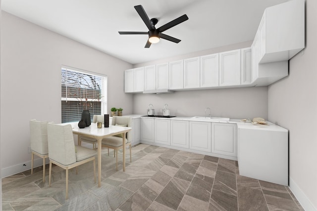 kitchen featuring baseboards, ceiling fan, light countertops, white cabinets, and a sink