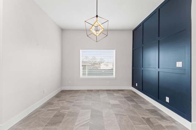 spare room featuring an inviting chandelier and baseboards