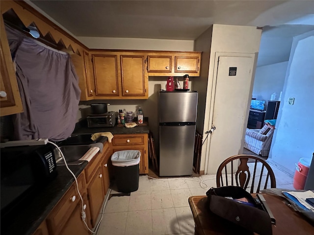 kitchen with black microwave, a toaster, freestanding refrigerator, brown cabinets, and dark countertops