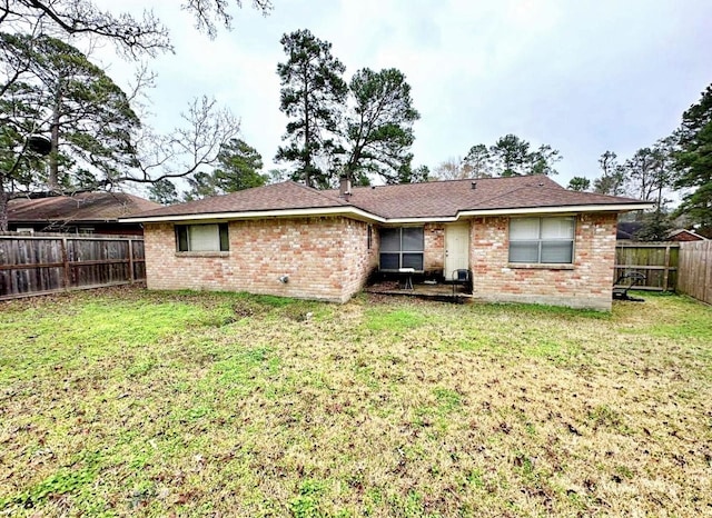 rear view of property with a fenced backyard, a yard, and brick siding