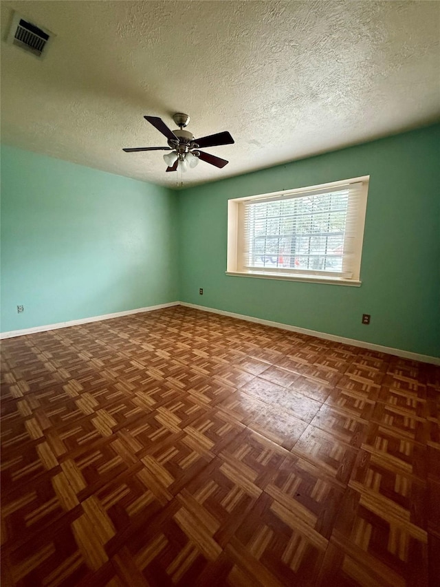 empty room featuring ceiling fan, a textured ceiling, visible vents, and baseboards