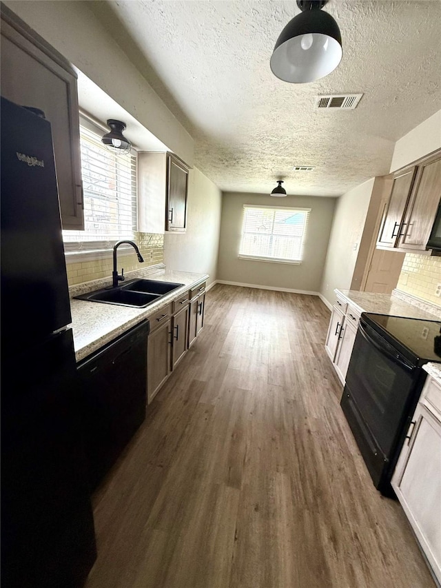 kitchen with black appliances, dark wood finished floors, a sink, and visible vents