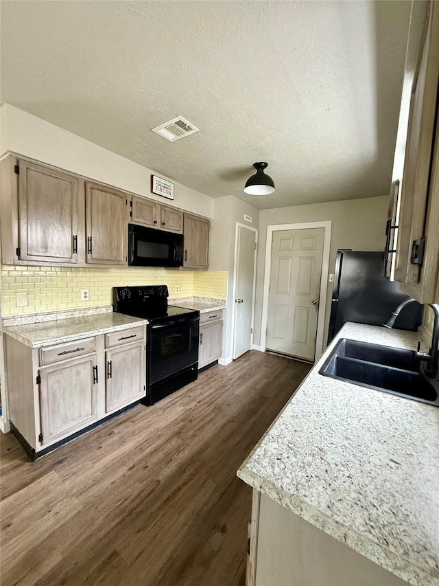 kitchen featuring light countertops, visible vents, dark wood-type flooring, a sink, and black appliances