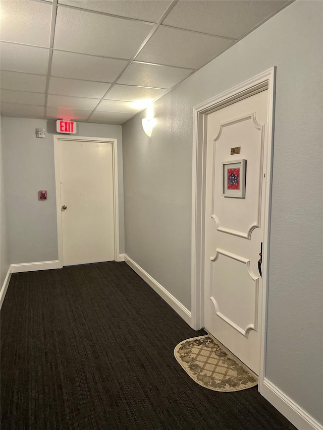 corridor with baseboards, dark colored carpet, and a drop ceiling