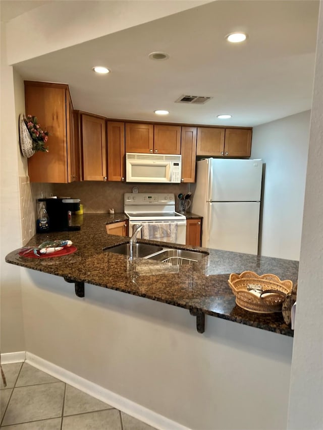 kitchen with light tile patterned floors, white appliances, a sink, visible vents, and dark stone countertops