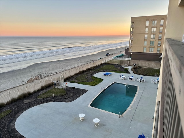 pool featuring a patio area, a beach view, fence, and a water view