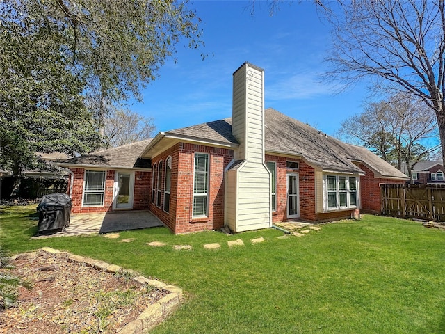 rear view of house with a lawn, a patio, fence, brick siding, and a chimney