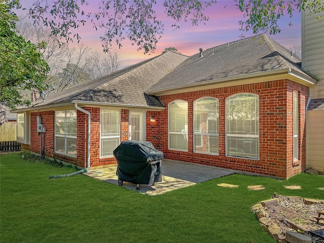 back of house featuring a patio, a yard, brick siding, and roof with shingles