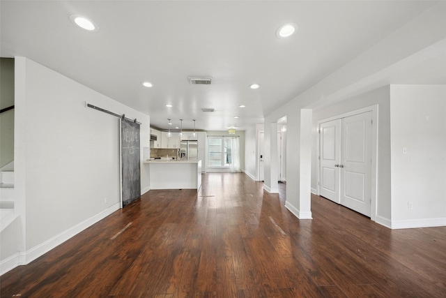 unfurnished living room with dark wood-style floors, visible vents, stairway, and a barn door