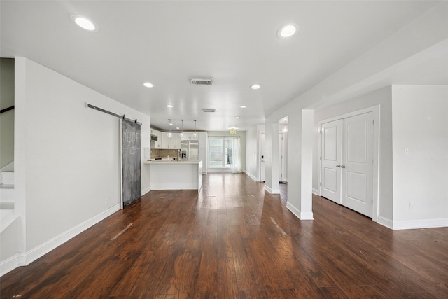 unfurnished living room with visible vents, baseboards, recessed lighting, a barn door, and dark wood finished floors