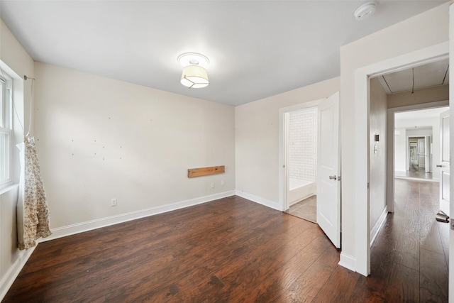 spare room featuring attic access, baseboards, and dark wood-style flooring