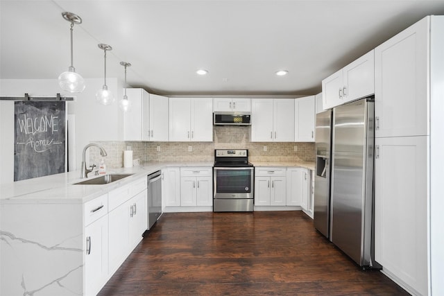 kitchen featuring backsplash, a barn door, light stone counters, appliances with stainless steel finishes, and a sink