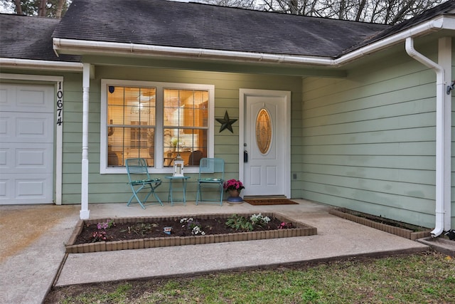 view of exterior entry featuring an attached garage, covered porch, and roof with shingles