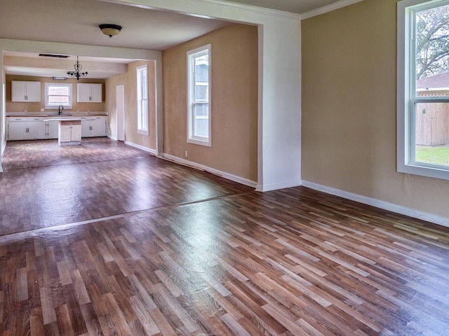 unfurnished living room featuring baseboards, dark wood-type flooring, a sink, and a healthy amount of sunlight