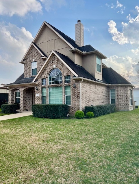 view of front of property featuring a front yard, brick siding, a chimney, and stucco siding