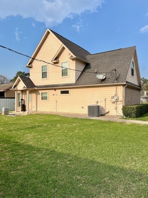 back of property with a patio area, roof with shingles, central AC, and a yard