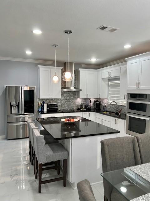 kitchen with stainless steel appliances, tasteful backsplash, visible vents, a sink, and wall chimney range hood