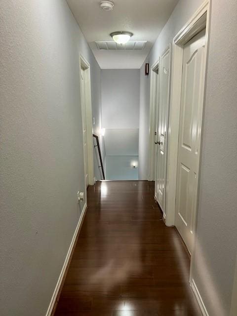 hall with dark wood-type flooring, baseboards, visible vents, and an upstairs landing