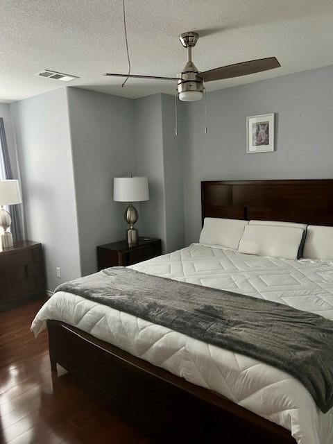 bedroom with a textured ceiling, visible vents, and wood finished floors