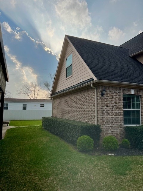 view of home's exterior featuring brick siding, a shingled roof, and a yard