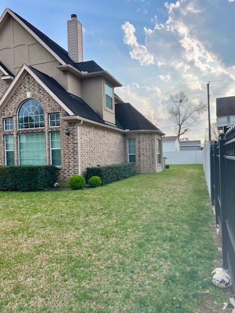 exterior space featuring a yard, brick siding, a chimney, and fence