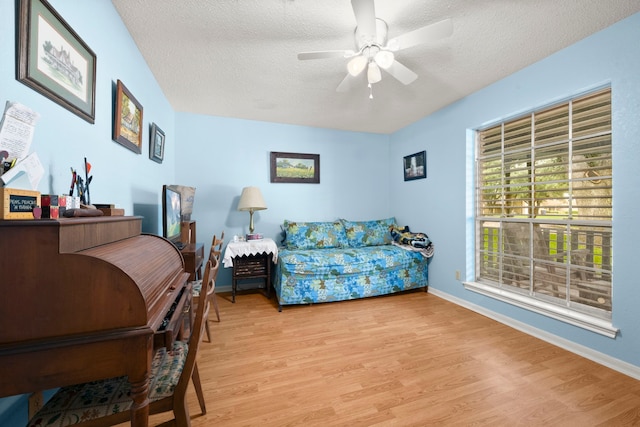 living area with baseboards, ceiling fan, a textured ceiling, and light wood finished floors