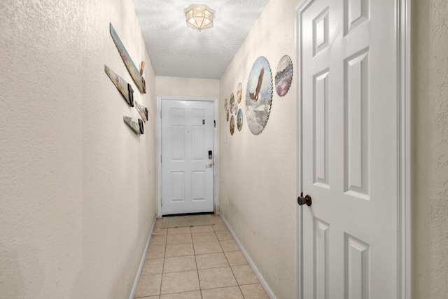 hall with light tile patterned floors, baseboards, a textured ceiling, and a textured wall