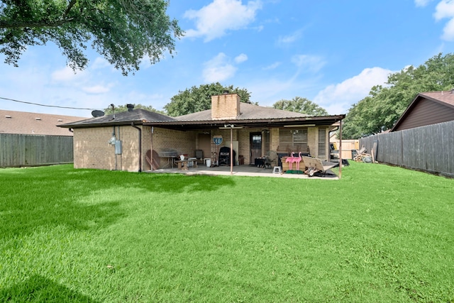 rear view of house with a patio, a fenced backyard, brick siding, a yard, and a chimney