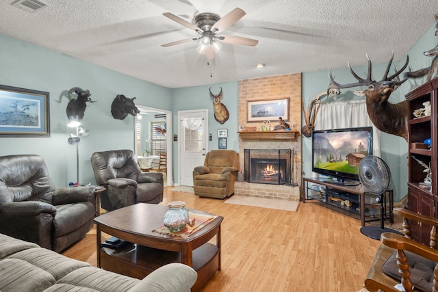 living room featuring a brick fireplace, visible vents, a textured ceiling, and wood finished floors