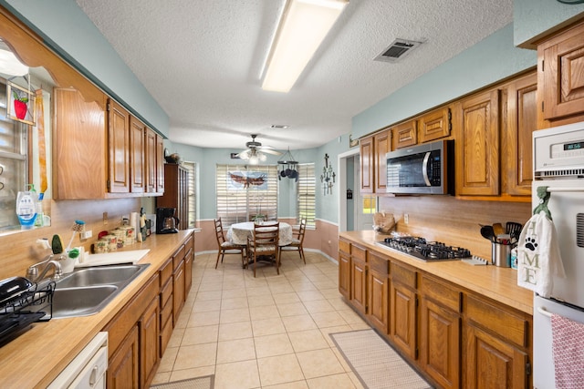 kitchen featuring brown cabinets, stainless steel appliances, backsplash, light tile patterned flooring, and a sink