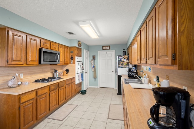 kitchen featuring brown cabinets, backsplash, appliances with stainless steel finishes, light tile patterned flooring, and a sink