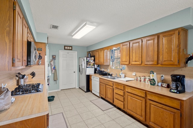 kitchen featuring light tile patterned floors, appliances with stainless steel finishes, brown cabinets, light countertops, and a sink