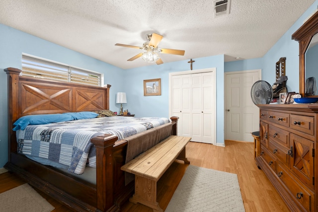 bedroom with ceiling fan, a textured ceiling, visible vents, a closet, and light wood finished floors