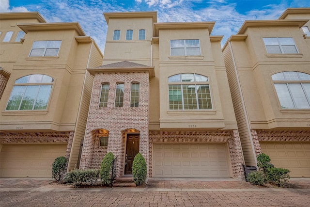 view of property featuring decorative driveway, an attached garage, and stucco siding